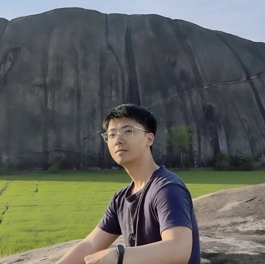 Binh Nguyen sitting on a rock in front of a granite mountain and green rice fields